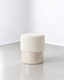 Helvis stool featuring a rounded ivory upholstered seat with a softly textured surface and a compact cylindrical base. Its simple sculptural profile combines tactile comfort with contemporary minimalist design.