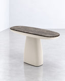 Hera X console table featuring a slim dark stone top with natural veining and a sculptural light-toned pedestal base. The contrast between the textured surface and rounded support creates a refined architectural accent.