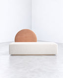 Horizon daybed sofa featuring an elongated upholstered base and a rounded terracotta-colored backrest cushion. The minimalist horizontal profile combines contemporary lounging functionality with a sculptural accent.