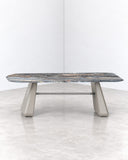Inge marble dining table featuring a richly veined grey stone tabletop with an organic elongated profile and sculptural light-toned supports. The natural stone pattern adds distinctive material character to the minimalist design.