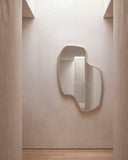 Sculptural LAB L mirror featuring a freeform silhouette and slim light-toned frame around a reflective surface. Its organic geometry adds depth and visual interest to refined interior spaces.
