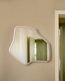 LAB M sculptural wall mirror with an asymmetrical silhouette and slim light-toned frame. Its organic geometry creates an elegant statement piece while maintaining a minimalist contemporary aesthetic.