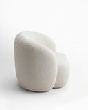 Side profile of the LYSA lounge chair showcasing its curved upholstered shell and generously padded seat. The organic silhouette combines sculptural form with an inviting, cocoon-like seating experience.