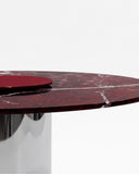 Close-up of the ORBITAE dining table showcasing the richly veined burgundy stone tabletop and polished metal pedestal base. The natural stone pattern emphasizes the table's luxurious sculptural character.
