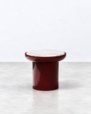 Romo side table featuring a rounded burgundy tabletop and a solid cylindrical pedestal base in a matching finish. Its compact monolithic form combines clean geometry with a bold contemporary color.