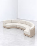 Serra sofa featuring a curved sectional configuration with generously padded neutral upholstery and a continuous low backrest. Its flowing silhouette creates a soft architectural presence in contemporary interiors.