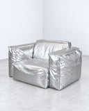 Sibylia armchair featuring a voluminous, softly structured seat and back upholstered in reflective silver-toned material. Its crinkled metallic finish gives the sculptural lounge chair a bold contemporary character.