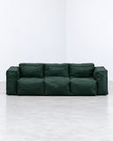 Sibylia sofa featuring deep green upholstered cushions arranged in a low, linear configuration with distinct segmented backrests. Its bold color and geometric proportions create a contemporary statement sofa.