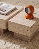 Close-up of the THERRA side table showcasing the textured light travertine surface and substantial stone construction. The natural material and monolithic form create a tactile contemporary accent piece.