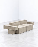 Tadao sofa featuring a modular arrangement of neutral upholstered seat and back cushions with clean rectangular forms. The low-profile design combines geometric simplicity with flexible contemporary seating.