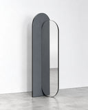 Takada floor mirror featuring a tall vertical reflective panel with a rounded arch top and contrasting dark and light-toned frame sections. Its clean geometric form creates a contemporary full-length mirror.