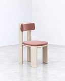 Taoto dining chair featuring a pink upholstered seat and backrest supported by contrasting light-toned wooden legs and a simple vertical back support. Its playful proportions combine tactile comfort with contemporary geometry.