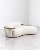 Tateyama chaise lounge featuring an elongated, organically curved upholstered seat with rounded ivory cushions and an integrated bolster. Its fluid silhouette creates a sculptural contemporary lounging piece.