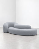 Trace Island sofa featuring a low-profile, curved upholstered seat in muted blue-grey fabric with softly rounded edges. The streamlined organic silhouette creates a contemporary focal point for relaxed lounge settings.