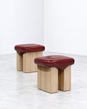 Wax stools featuring rounded burgundy upholstered or finished seats supported by chunky cylindrical light-toned wooden legs. The contrast between the rich red tops and natural wood bases creates a playful contemporary seating set.