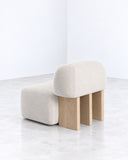 Yemeni lounge chair featuring a rounded upholstered seat and backrest supported by solid light-toned wooden legs. The contrast between tactile neutral upholstery and geometric timber supports creates a refined contemporary design.