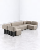 Yemeni sofa featuring a modular arrangement of neutral upholstered cushions and backrests supported by contrasting dark and light-toned block legs. The geometric construction combines soft seating with architectural detailing.