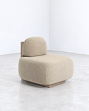Yoshida lounge chair featuring a rounded upholstered backrest and deep cushioned seat in textured beige fabric. Its compact, softly sculptural form emphasizes comfort and understated contemporary design.
