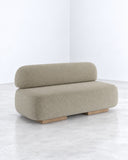 Yoshida sofa featuring a low rectangular upholstered seat and softly rounded backrest in textured beige fabric. Its understated silhouette and tactile upholstery emphasize contemporary comfort and minimalist design.