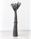 Sandrine Herlin Baobab Noir Tall Lighting features an elongated, tapered dark body with an irregular textured surface and delicate branching stems. Its slender, tree-inspired silhouette and subtle warm accents make it a striking sculptural lighting piece for contemporary interiors.