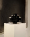 Montée black sculptural vessel displayed as a statement object with bold geometric proportions. Its glossy finish and tiered form bring contemporary character to refined interiors.