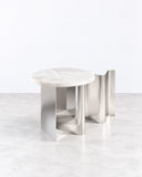 Sketch side table featuring a pale rounded tabletop with subtle natural veining and a sculptural reflective metal base. Its fluid supports and minimalist silhouette create a refined contemporary accent table.