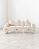 Sculptural Lighting Sofa featuring cream upholstered seating, a distinctive zigzag geometric base, and pointed backrest detailing. The architectural silhouette combines bold contemporary design with a soft, neutral finish.