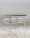 Looking Glass Cabinet showcasing a polished metal frame, glass panels and integrated shelving. Designed as a statement storage piece for sophisticated modern interiors.