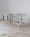 Troy Smith Looking Glass Cabinet featuring rounded metal framing and transparent glass shelving. Its architectural silhouette brings a refined contemporary character to luxury interiors.