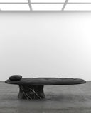 Off Balance Daybed showcasing a low sculptural profile, black upholstery and a distinctive marble pedestal base. Designed as a statement lounge piece for sophisticated modern interiors.