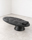 Sculptural Off Balance daybed featuring a black tufted upholstered cushion and an asymmetrical pedestal base with a dark veined stone finish. Its elongated profile and contrasting materials create a distinctive contemporary lounging piece.