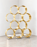 Sculptural Whole Book Shelf featuring stacked circular metallic rings in a polished gold finish, creating an open geometric storage structure. The modular-looking composition combines functional book display with bold contemporary design.