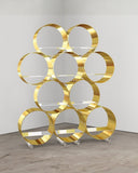 Troy Smith The Whole Brass Shelf showcasing polished brass circular forms with transparent glass shelves and metal supports. A statement shelving system for sophisticated modern interiors.