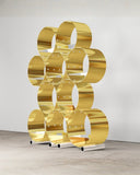 The Whole Brass Shelf featuring layered cylindrical brass compartments and transparent glass shelving. Its sculptural geometric design creates a distinctive storage piece for contemporary interiors.