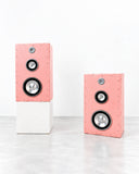 YONT Brutalist Pink Speakers XL featuring a pair of bold rectangular speaker cabinets in textured pink, with exposed circular drivers and contrasting metallic details. Their clean geometric forms and expressive colour combine audio functionality with contemporary sculptural design.