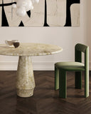 Round marble table with a green chair in a room with abstract art on the wall.