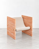 Adri lounge chair featuring a sculptural orange travertine frame with integrated armrests and a contrasting white seat cushion. The natural stone texture and geometric construction create a distinctive contemporary accent chair.
