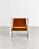 Adri lounge chair featuring a warm metallic frame, angular armrests, and a rich pistachio-toned upholstered seat and backrest. The clean geometric structure combines contemporary materials with a distinctive color accent.