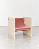 Adri lounge chair featuring a light travertine frame with integrated armrests and a muted rose upholstered seat and backrest. The contrast between natural stone and soft upholstery creates a sculptural contemporary chair.