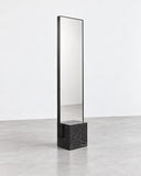 Full-length CoExist mirror with a narrow vertical reflective panel and a solid dark Nero stone base. The minimalist frame and monolithic base emphasize contemporary architectural design.