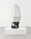 Lella mirror featuring a rounded vertical reflective panel set into a bold Grand Antique marble base with contrasting black and white veining. The sculptural stone support combines natural patterning with contemporary design.