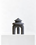 LS-03 volcanic rock sculpture featuring a tiered, temple-like silhouette with a stepped pointed top and arched base. Its porous charcoal surface highlights the natural texture of volcanic stone.