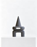 LS-04 volcanic rock sculpture featuring a pointed conical top, a rounded central opening, and a sturdy arched base. The rough charcoal stone surface creates a striking contrast with the object's simple geometric form.