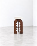 METAMO Arcano Bench featuring a pale rectangular seat supported by a sculptural arched wooden base with distinctive cutout detailing. Its contrasting finishes, visible wood grain, and architectural form create a refined contemporary seating piece.