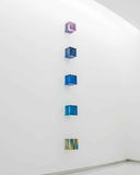 Linear installation of 11 square wall sculptures fading from blue to beige