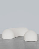 Two white, wavy, abstract sculptures on a gray surface with a light gray background
